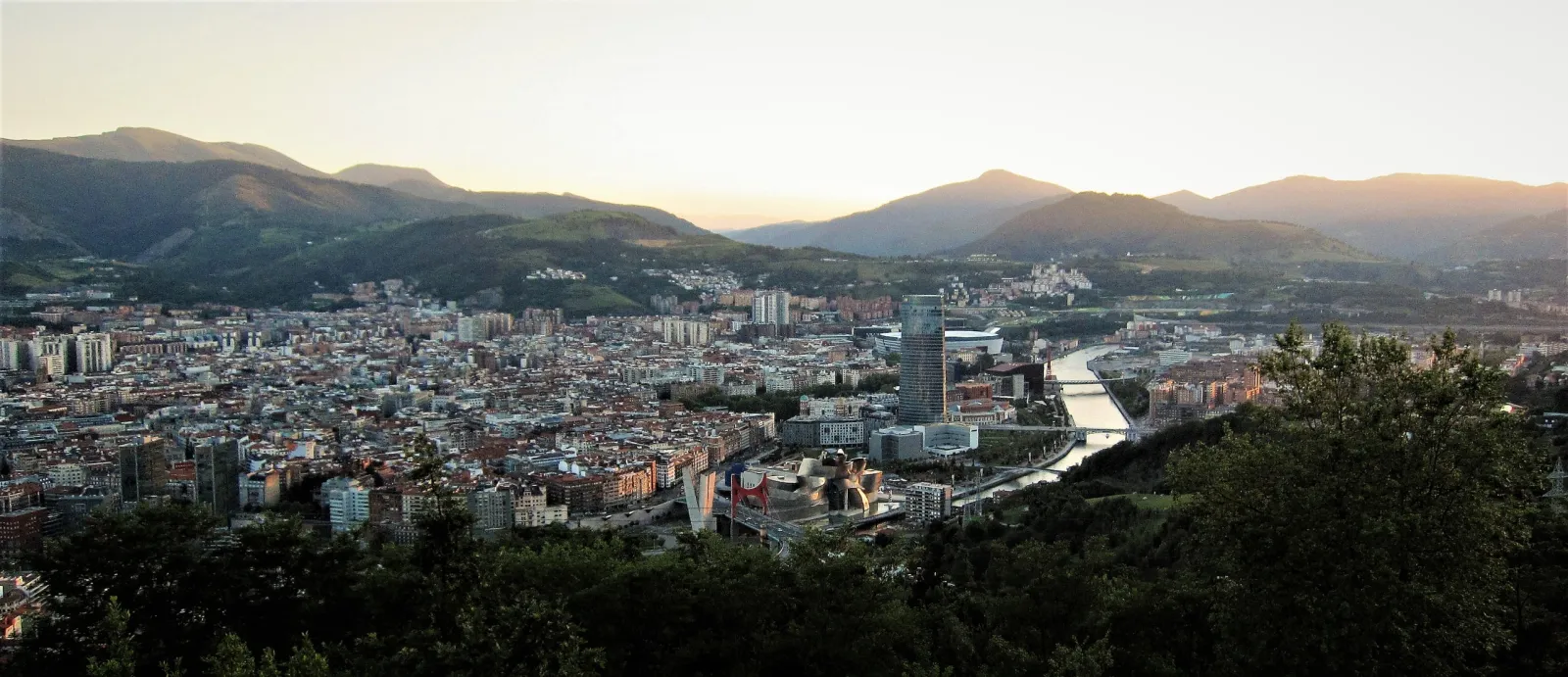 Bilbao at sunset seen from the Artxanda viewpoint, with the Guggenheim Museum, the Iberdrola tower and the Nervión estuary among green hills